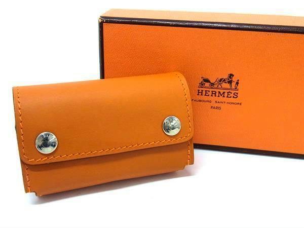 Orange leather domino case with two silver snap closures displayed in front of an orange Hermès box.