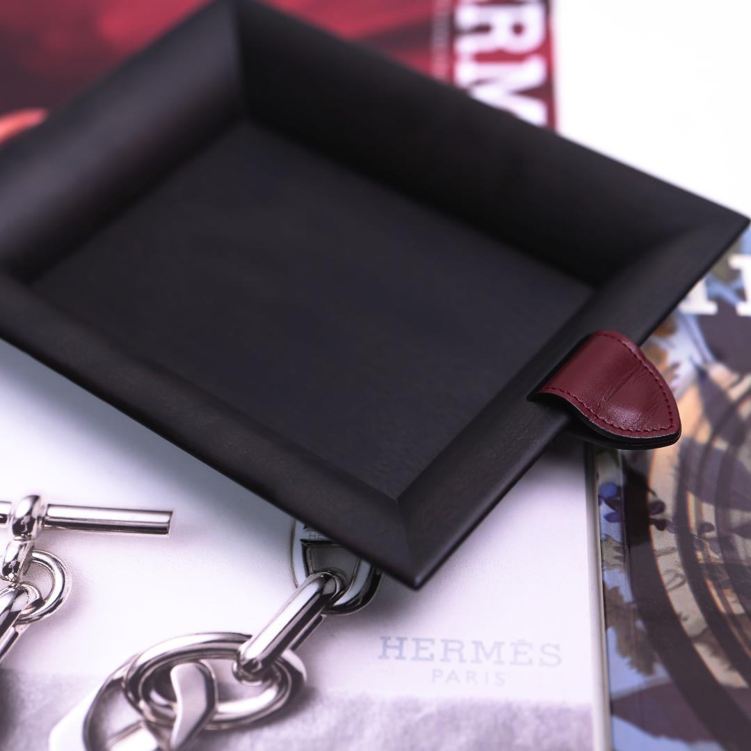Black wooden tray with a red leather tab resting on printed magazine pages.