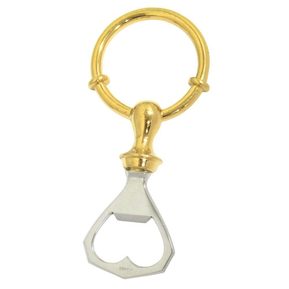 Gold and silver HERMES stainless steel bottle opener with heart-shaped opening and round keyring on a white background.