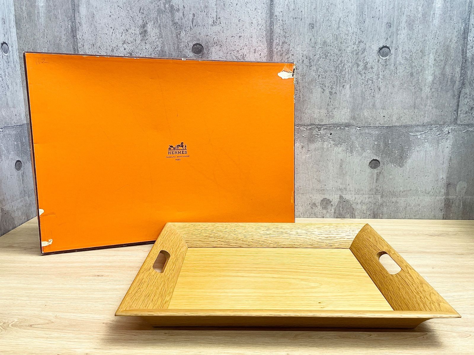 Beige wooden kitchen tray with cutout handles shown in front of an orange box.