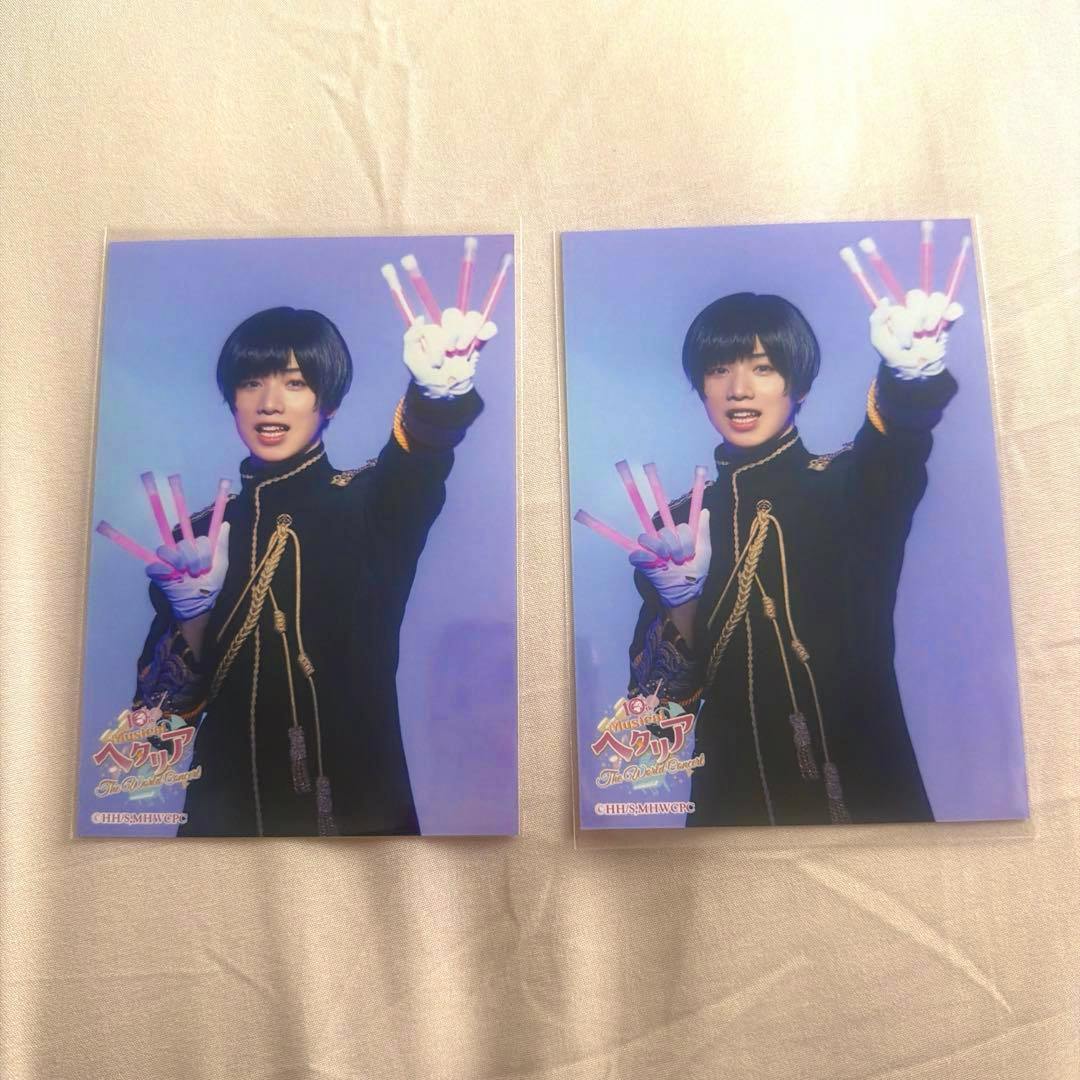 Two printed photo cards of the Hetalia stage musical's Japan character placed side-by-side on a light fabric surface.