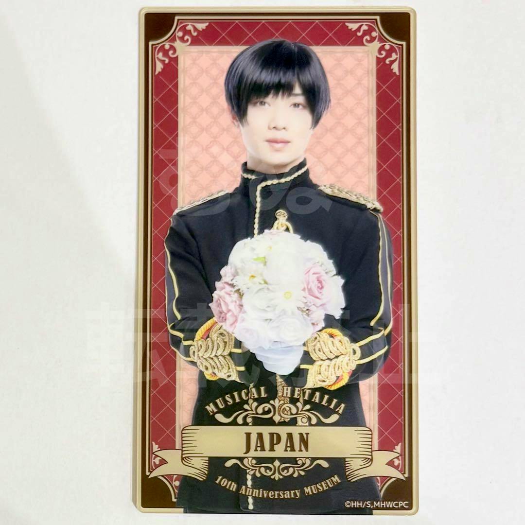 Rectangular acrylic plate showing the Japan character from Musical Hetalia in a black uniform holding a bouquet, with a decorative border and a banner reading "JAPAN".