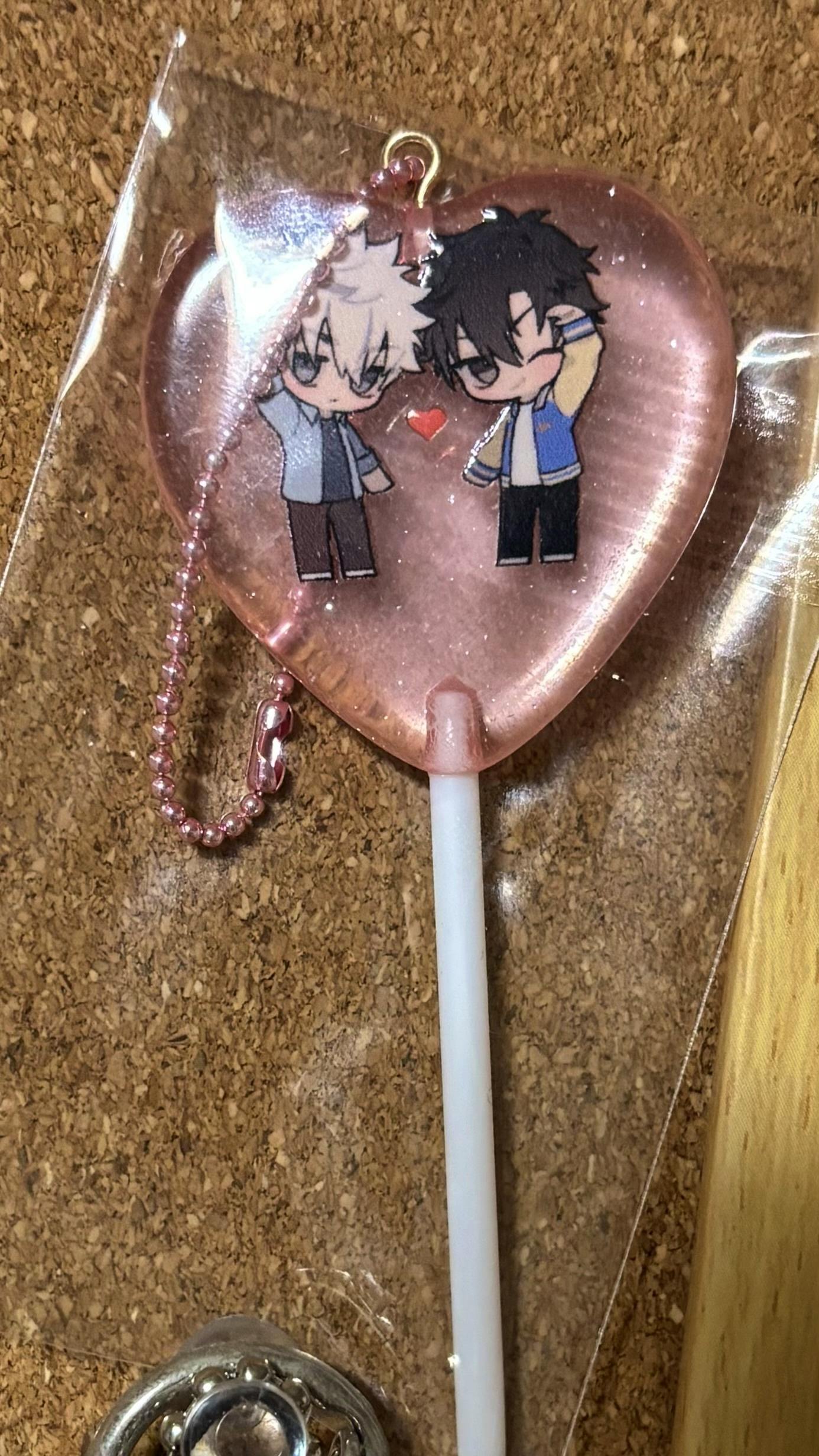 Close-up photo of the pink heart-shaped acrylic keychain showing two chibi characters and an attached pink ball chain.