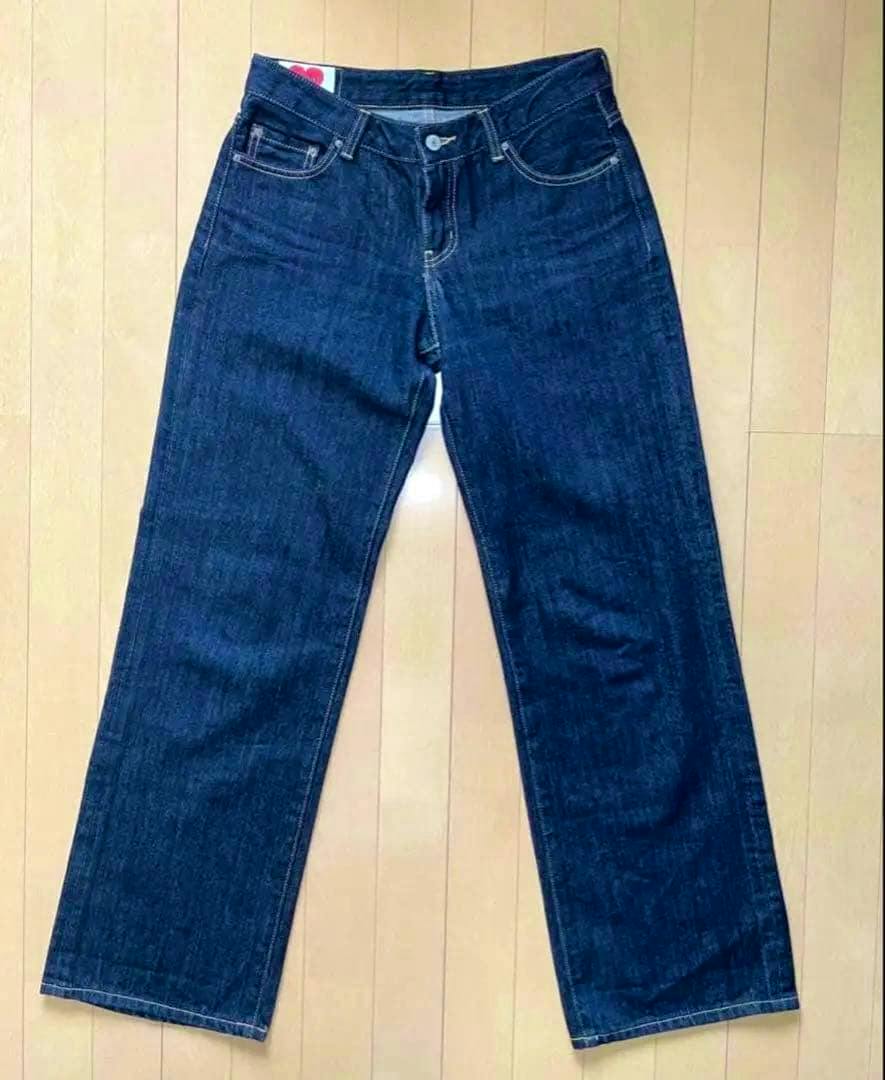 Front view of dark blue denim women's pants laid flat on a wood floor.