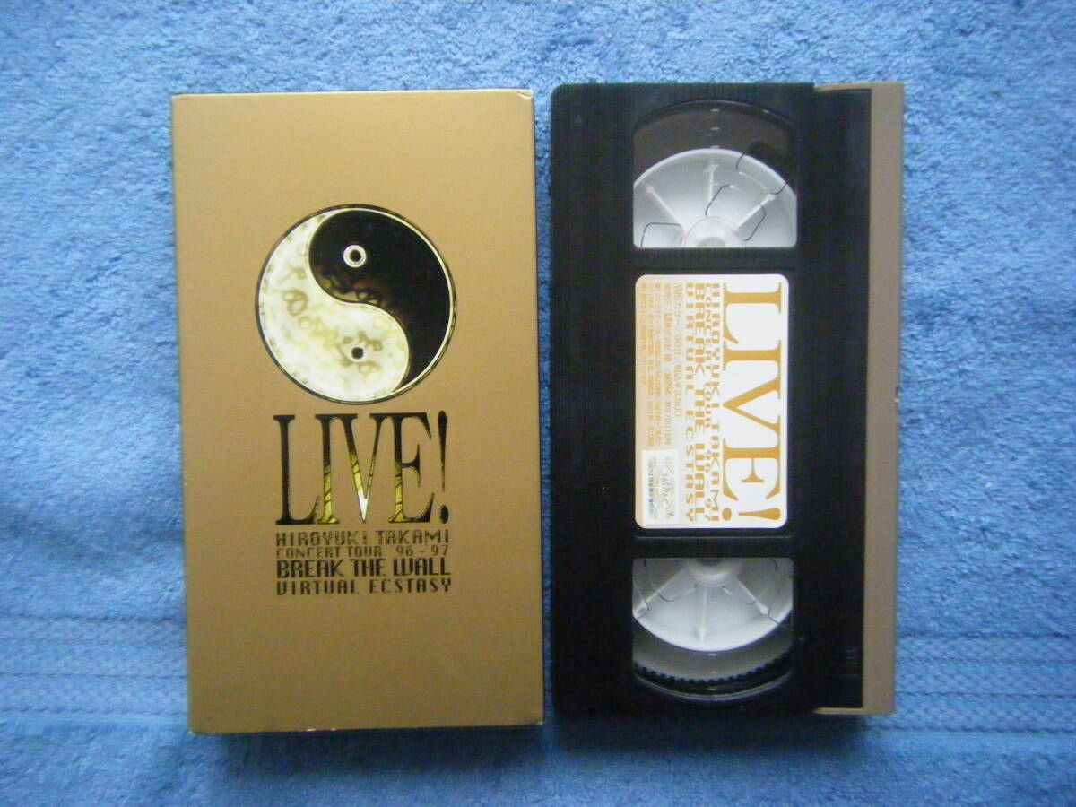 VHS tape labeled "LIVE!" next to its gold slipcover, both on a blue towel.