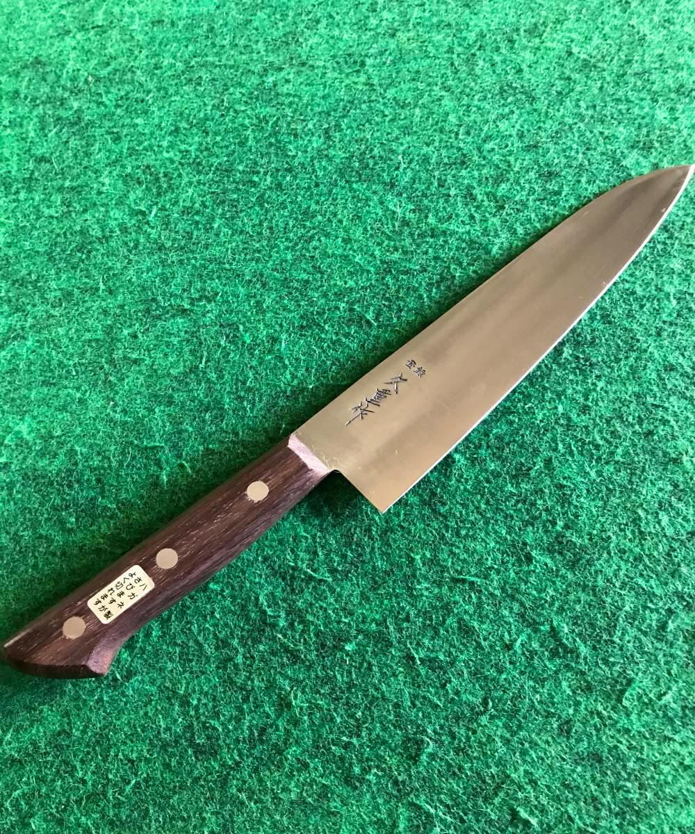 A SK steel 180mm chef knife with a wooden riveted handle lying on green felt.