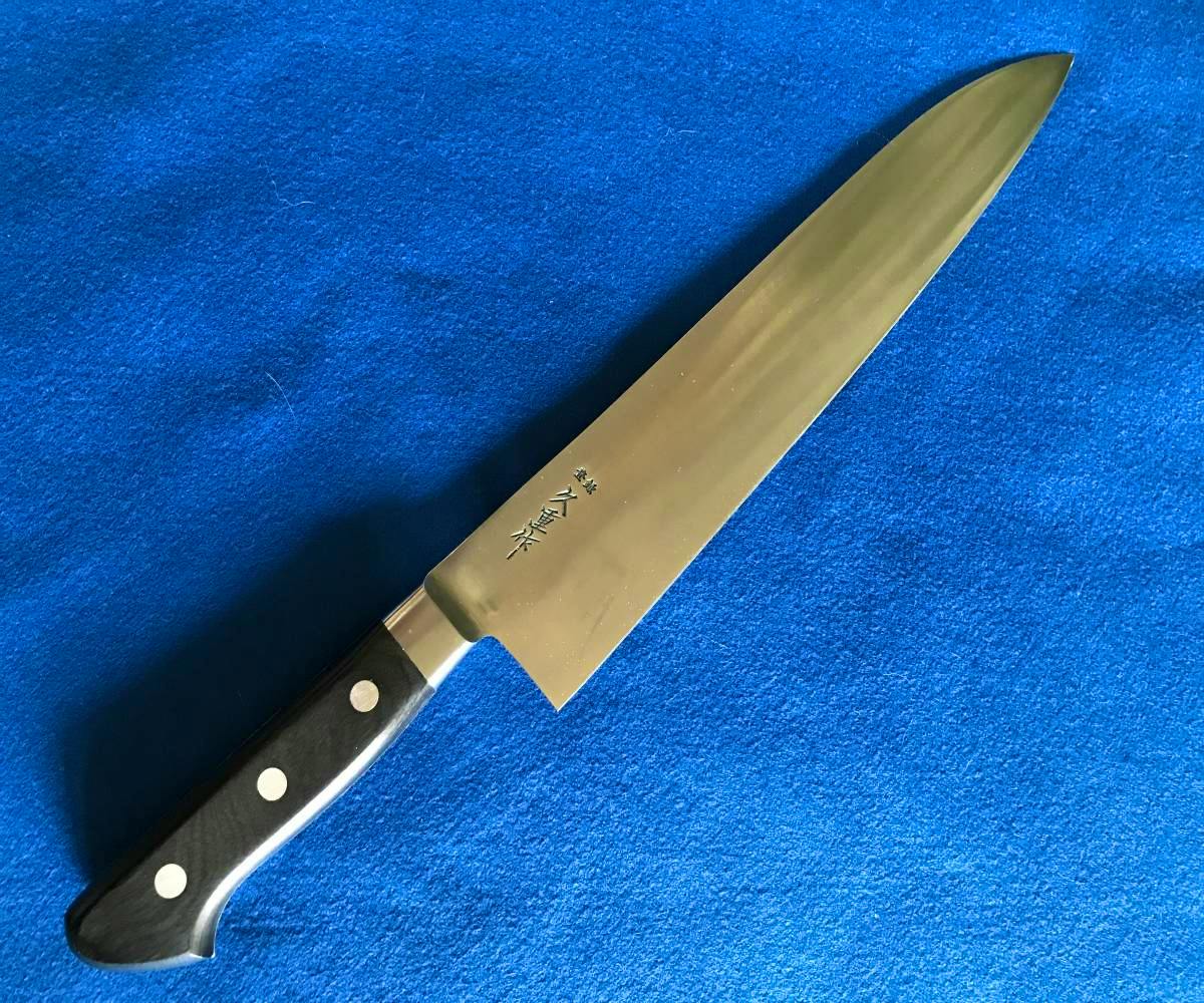 A SK steel 210mm chef (gyuto) knife with a stainless-steel blade bearing Japanese markings and a black three-riveted handle on a blue background.