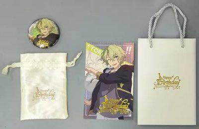 Birthday set laid out on a gray background showing a round badge, a small drawstring pouch, a character illustration card, and a paper gift bag.