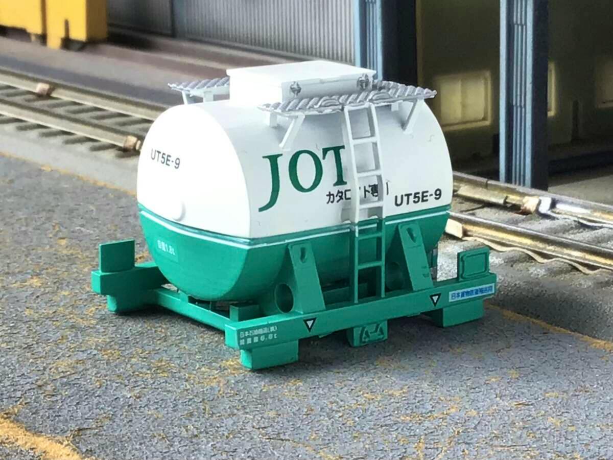 Close-up of a HO-scale UT5E-9 tank container model in white and green sitting on a model railway surface.