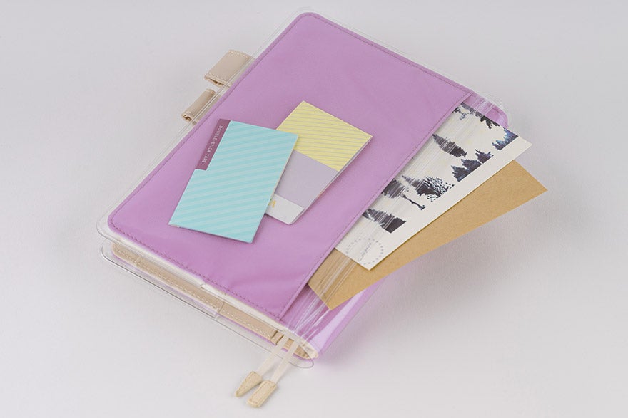 Purple translucent Hobonichi cover-on-cover placed over a planner with cards and papers tucked inside.
