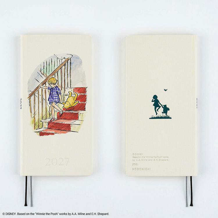 Two cream-colored 2027 Hobonichi diaries shown front and back; the front shows an illustration of a child and Winnie-the-Pooh on stairs and the back shows a silhouette of a child and Pooh.