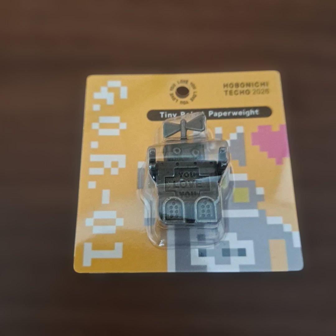 Front view of the product packaging showing a small robot paperweight attached to a yellow backing card.