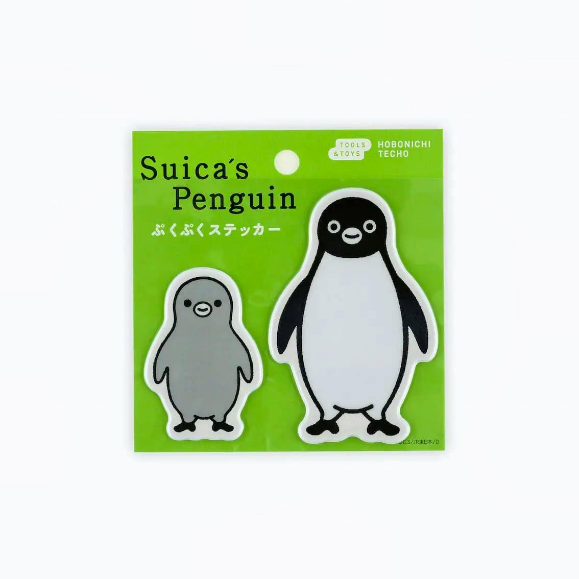 Two Suica Penguin puffy stickers (a small gray chick and a larger black-and-white penguin) shown on green backing packaging.