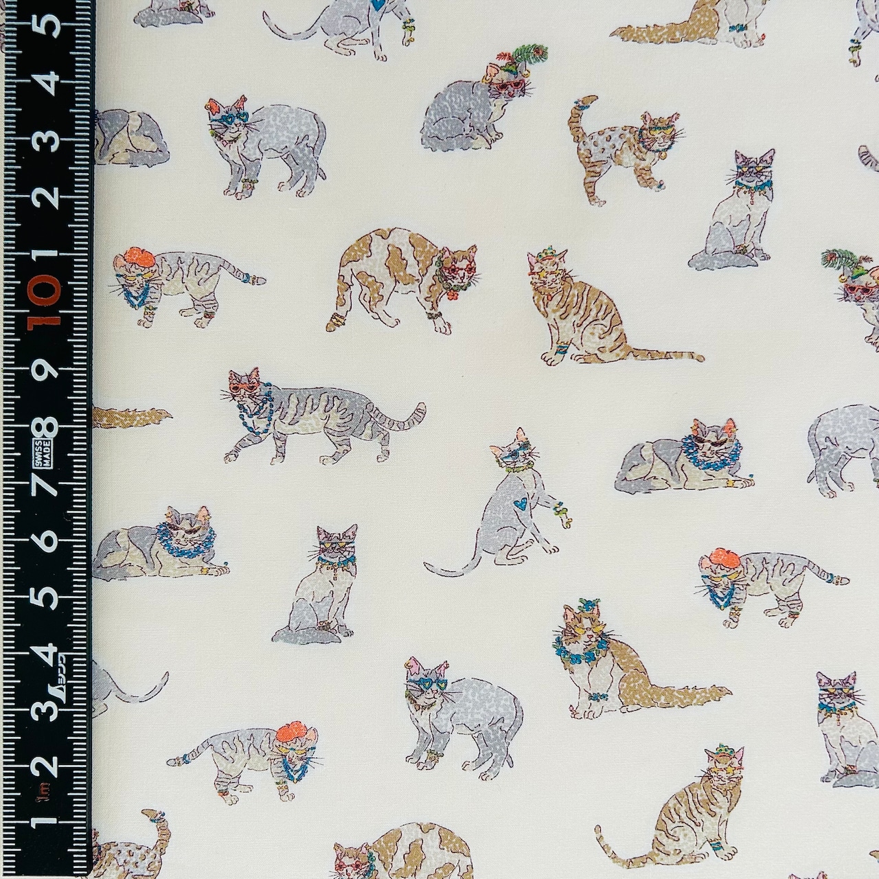Close-up of cotton fabric printed with small illustrated cats with a ruler at the left showing scale.