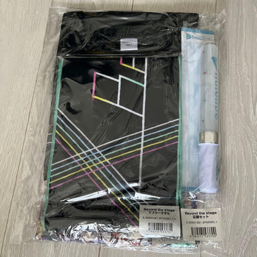 Packaged Beyond the stage muffler towel, folded black T-shirt, and penlight in clear plastic on a wooden floor.