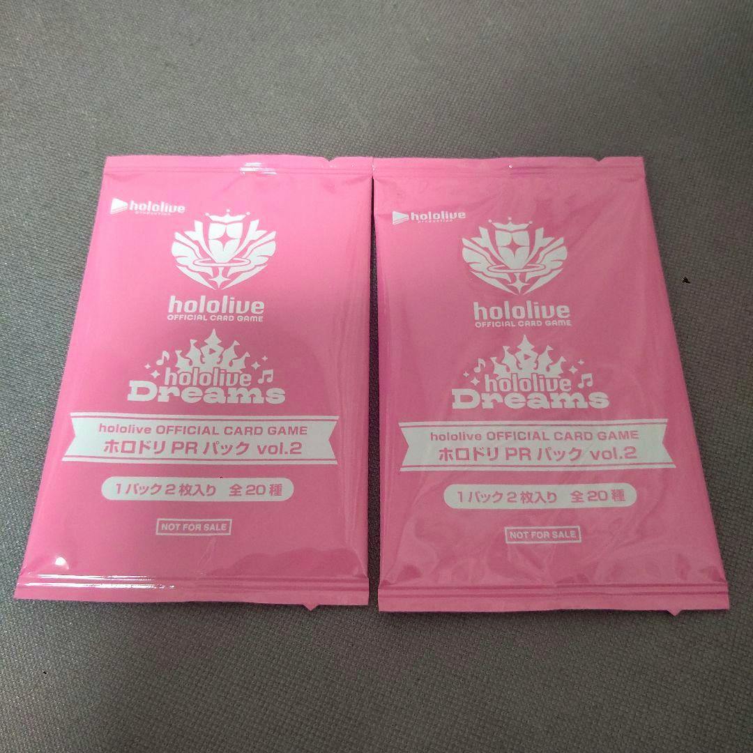 Two pink sealed Hololive Official Card Game PR Pack vol.2 pouches lying side by side on a gray surface.