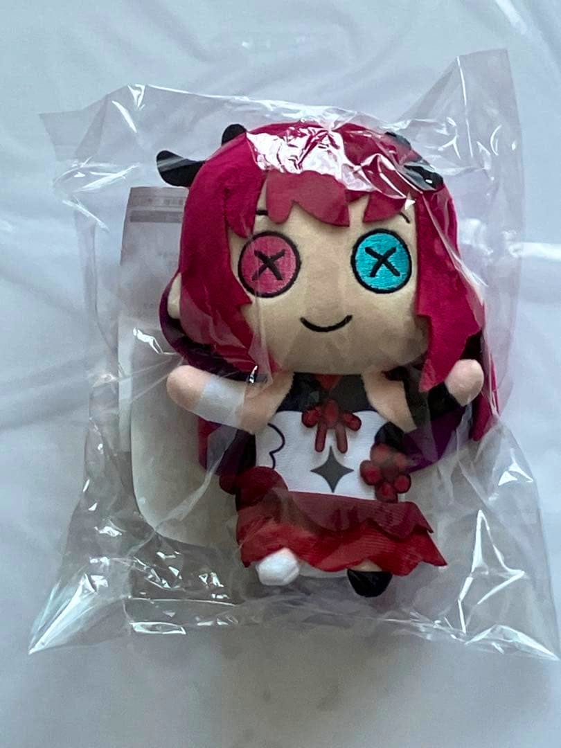 Front view of the Hololive IRyS The Plush KeychainRyS plush keychain in clear plastic packaging, showing the character's pink hair, mismatched stitched eyes, and red-and-white outfit.