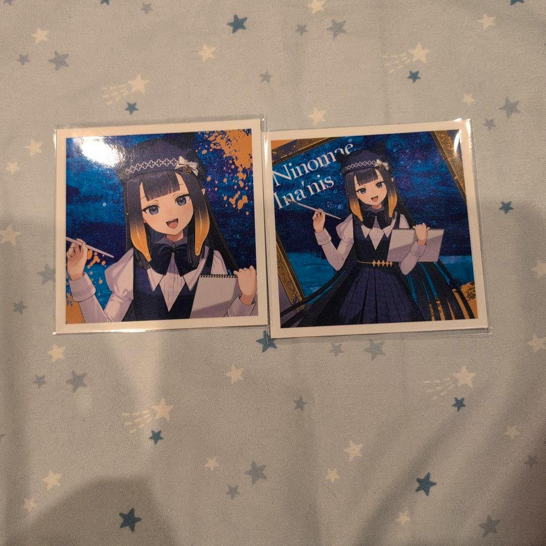 Two laminated photocards of the Hololive character Ninomae Ina'nis placed side by side on star-patterned fabric.