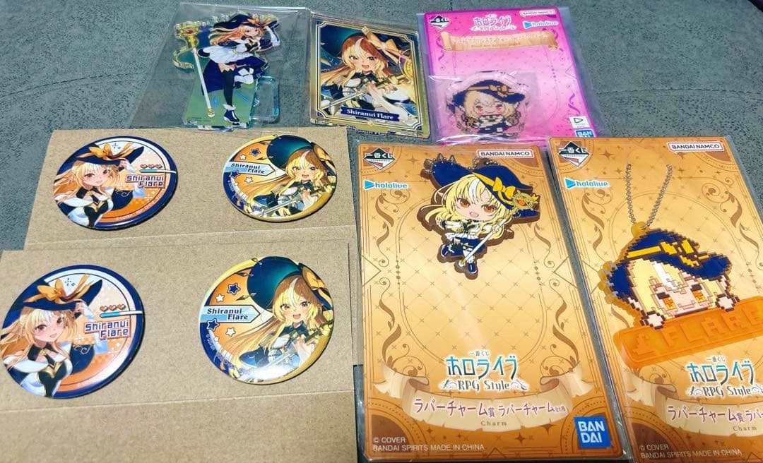 Photo of a Hololive Shiranui Flare goods set showing multiple character badges, an acrylic standee, and packaged rubber/pixel charms.