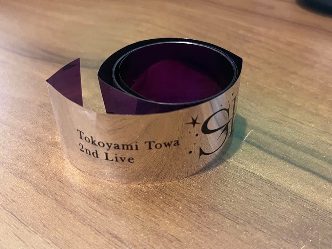 A rolled silver concert tape printed with "Tokoyami Towa 2nd Live" resting on a wooden surface.
