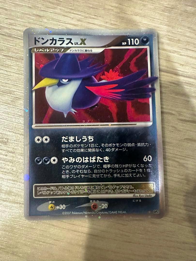 Front of the ドンカラス Lv.X trading card showing the card artwork and Japanese text on a wood surface.