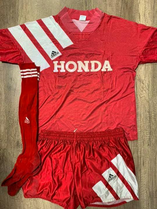 Red HONDA jersey with matching red shorts and red socks laid flat on a wooden floor.