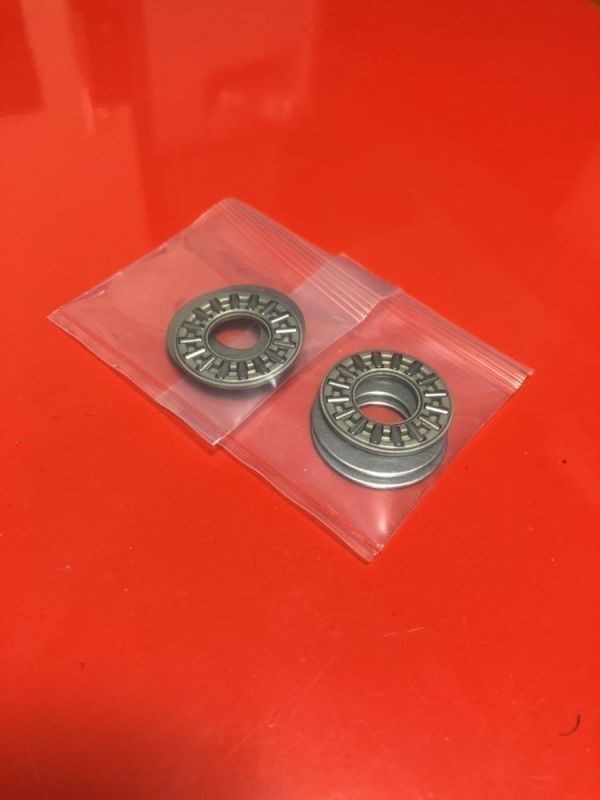 Two front fork spring thrust bearings for a motorbike, each in a clear plastic bag on a red surface.