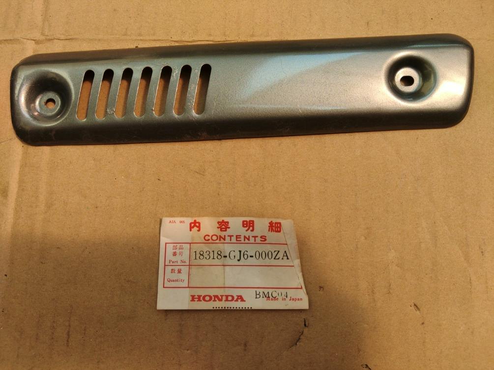 Metal muffler (silencer) cover shown on cardboard with a Honda part label reading 18318-GJ6-000ZA.