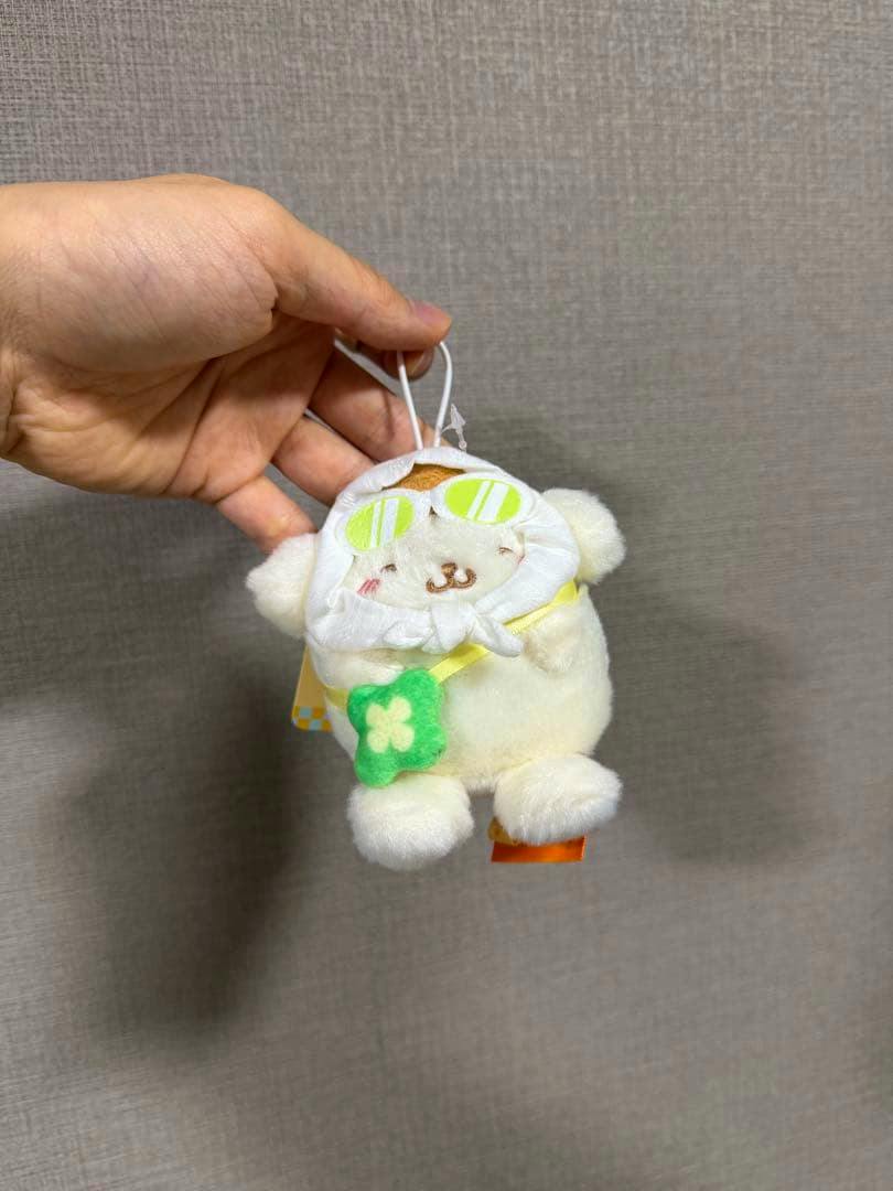 Front view of the Pompompurin 30th anniversary Hong Kong limited plush mascot wearing a hood, held by a hand.