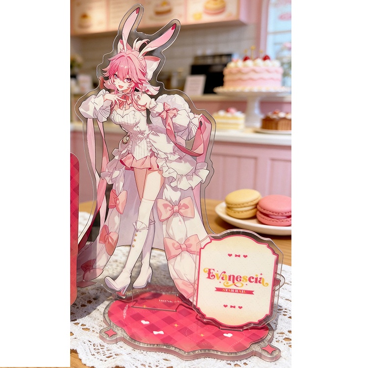 Acrylic stand showing a pink-haired, bunny-eared character on a decorative base displayed on a table with cakes and macarons in the background.