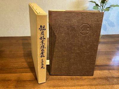 Brown hardcover book and beige slipcase standing on a wooden table.