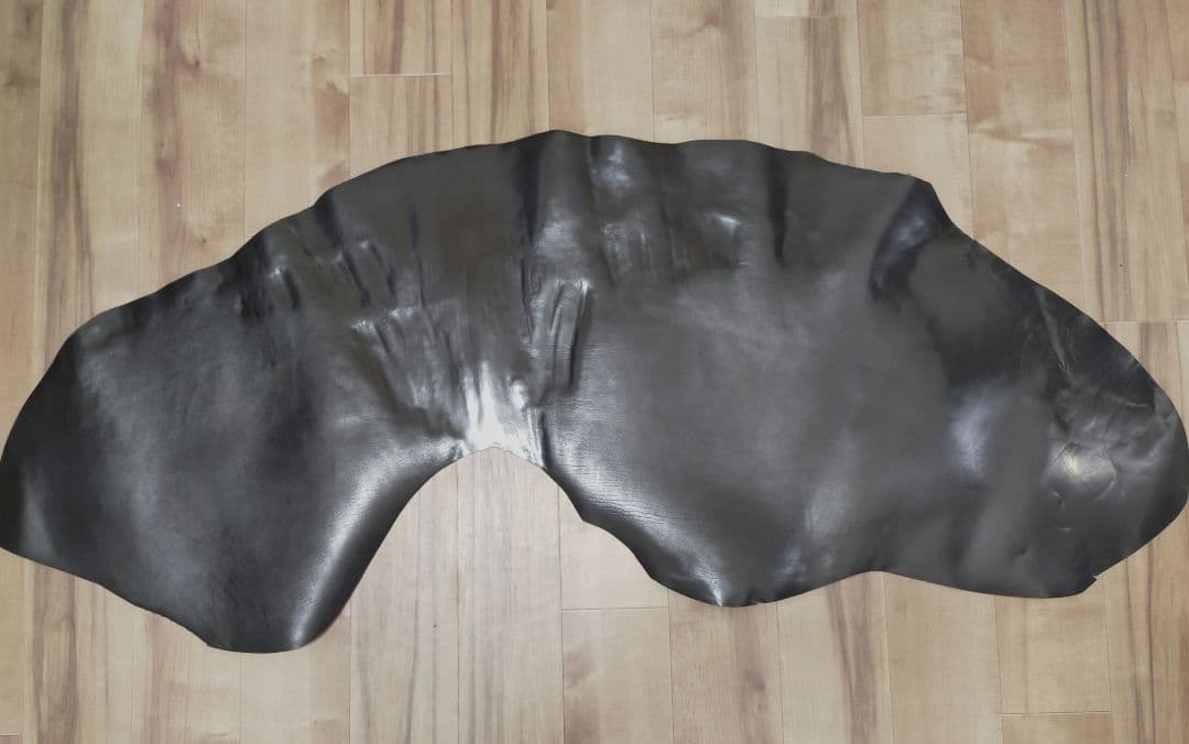 A black horse leather hide laid flat on a wooden floor.