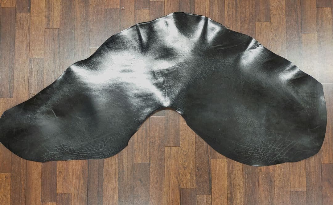 A large black horse leather hide laid flat on a wood floor.