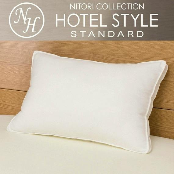 White hotel-style inflatable pillow on a bed against a wooden headboard with HOTEL STYLE STANDARD text above.
