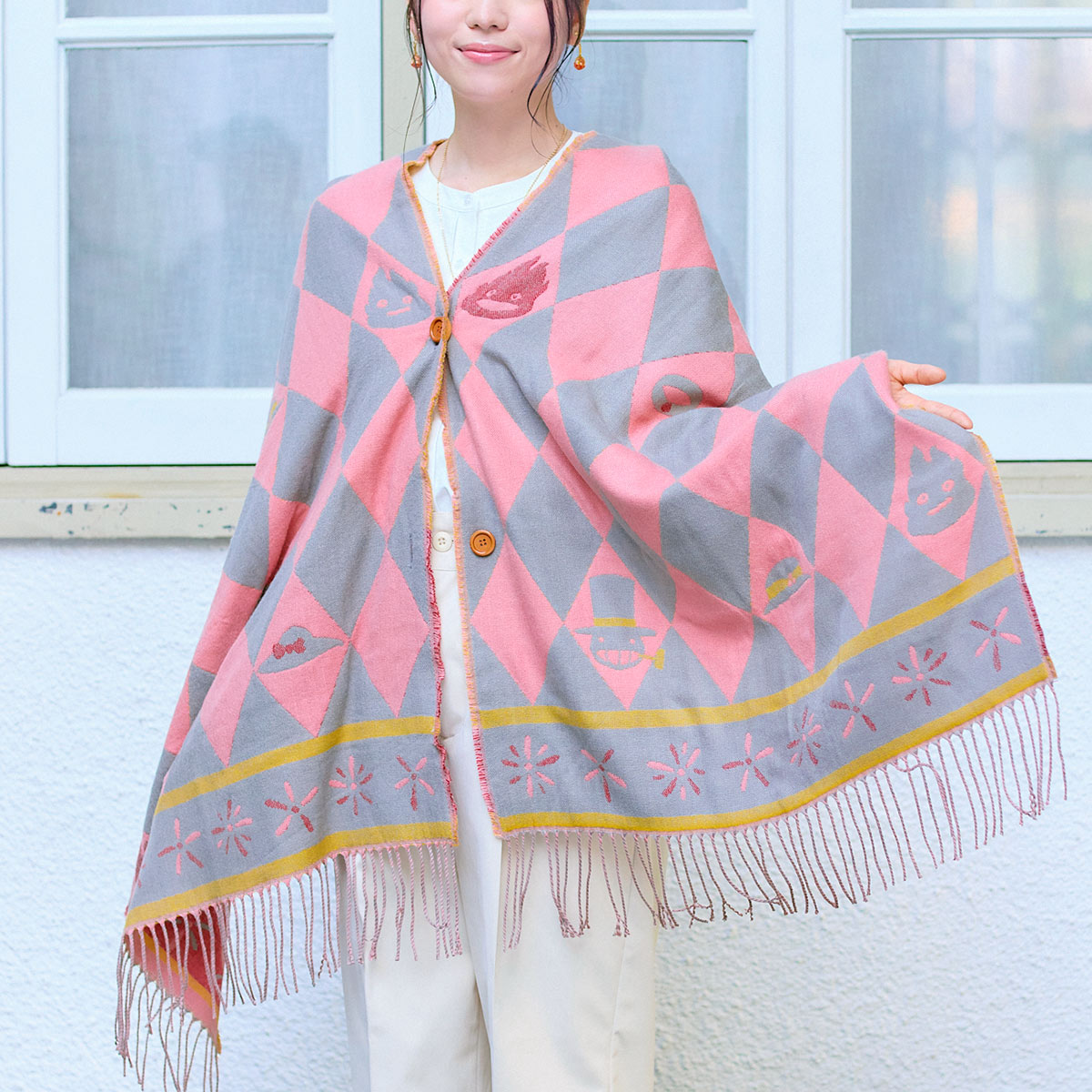 Woman wearing an acrylic buttoned scarf (stole) in a pink and gray diamond pattern with fringe.