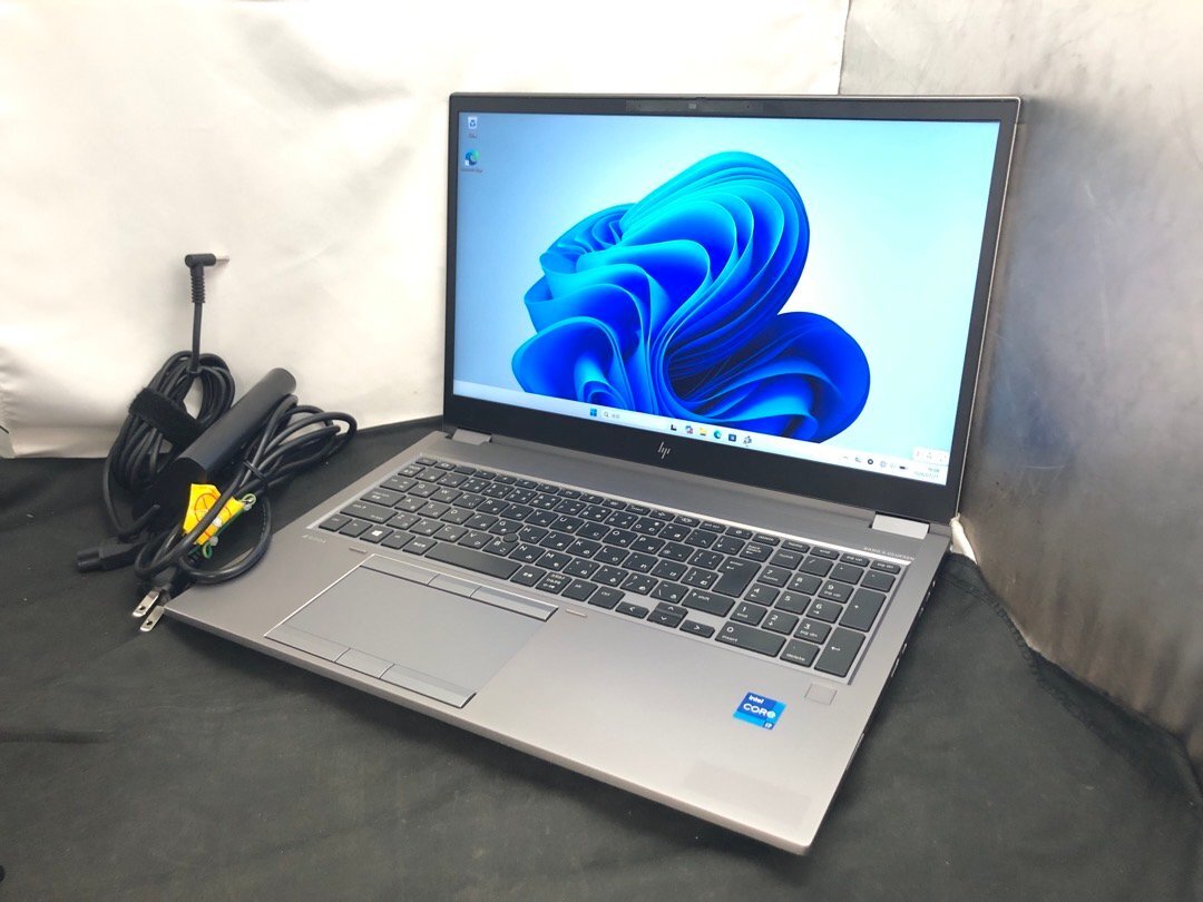 Silver HP ZBook Fury 15.6-inch laptop open on a surface showing Windows 11 on the screen with its power cord beside it.