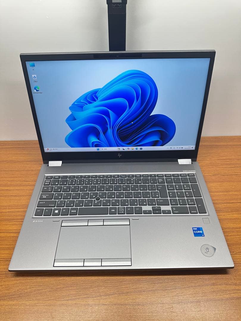 Open HP laptop on a wooden surface showing the display with a Windows desktop, keyboard, and touchpad.