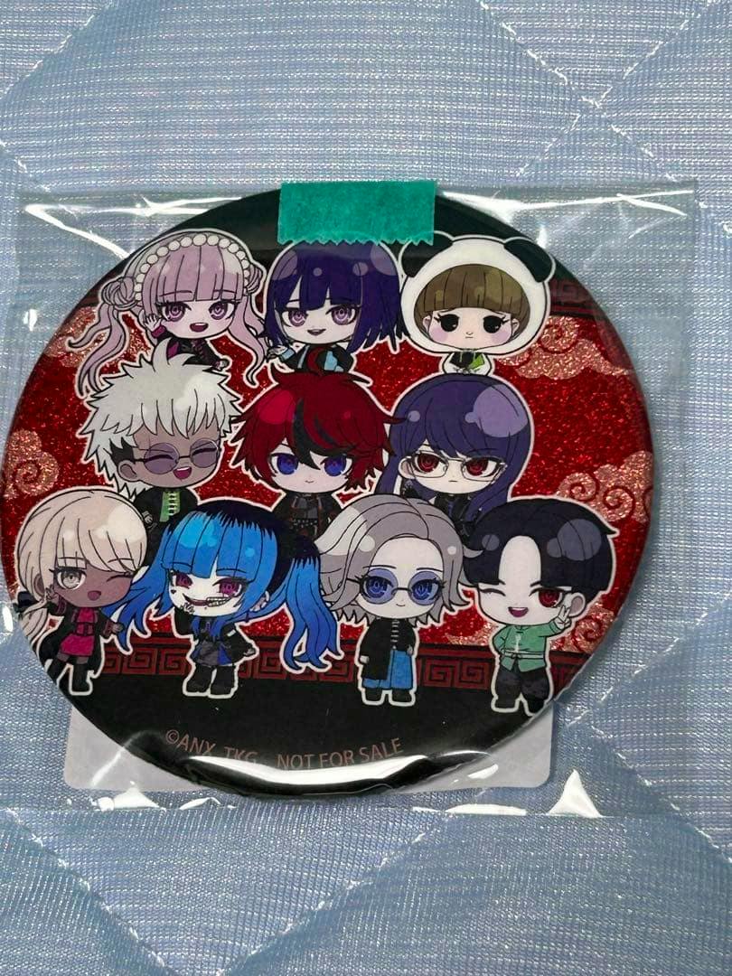 Front photo of a round can badge in plastic packaging depicting chibi characters on a red patterned background.