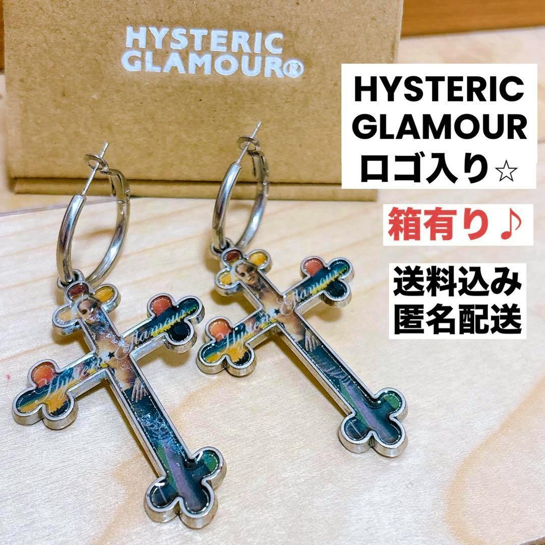 Pair of Hysteric Glamour cross hoop earrings placed on a light wood surface with a HYSTERIC GLAMOUR box visible behind them.