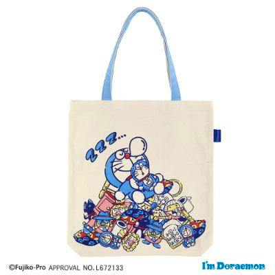 Beige tote bag with blue handles showing a pile of sleeping Doraemon characters printed on the front.