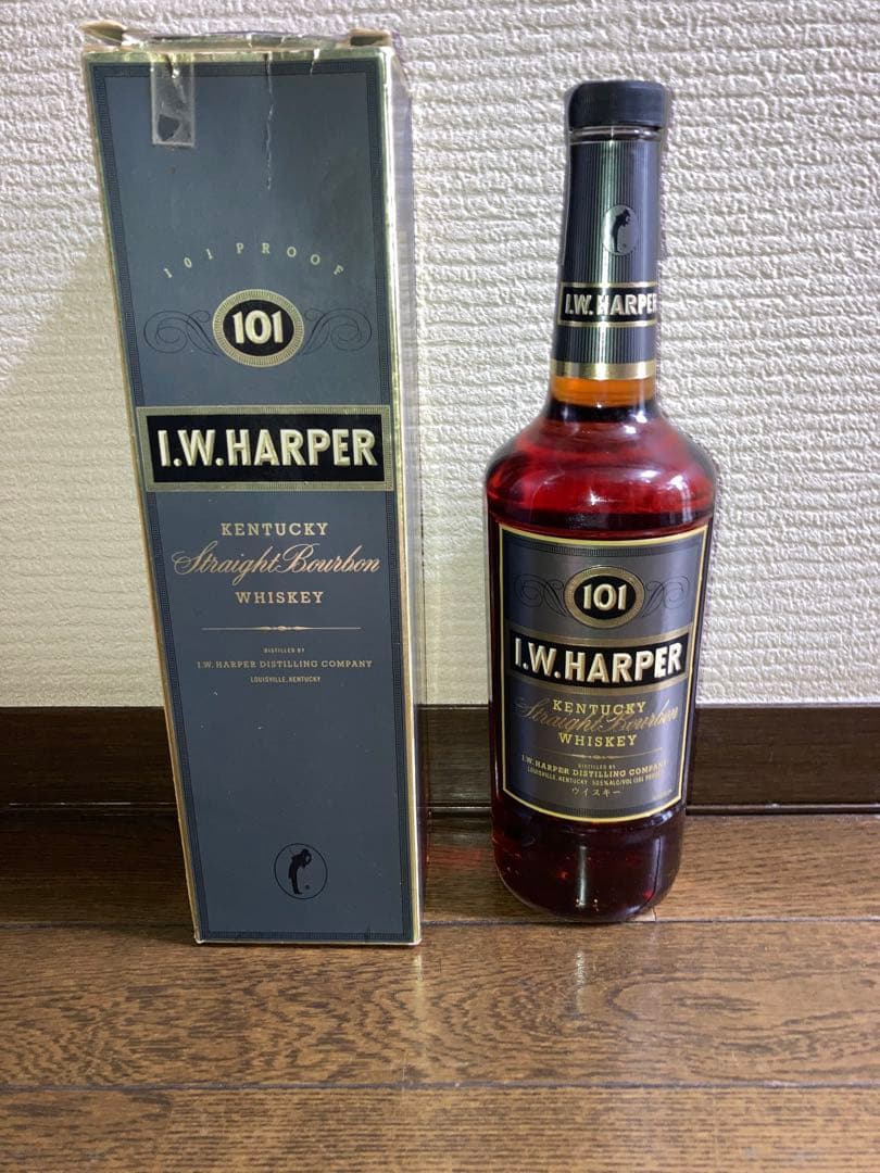 A bottle of I.W. Harper 101 bourbon whiskey standing next to its box on a wooden floor.
