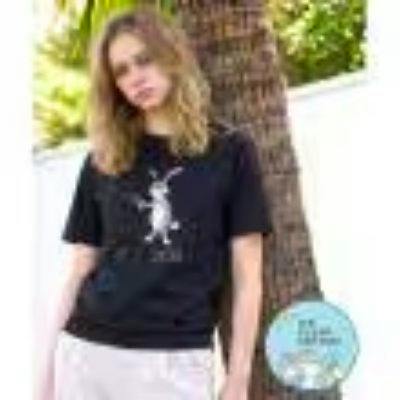 A model wearing a black cotton T‑shirt with a white pistol-rabbit graphic standing outdoors by a tree.
