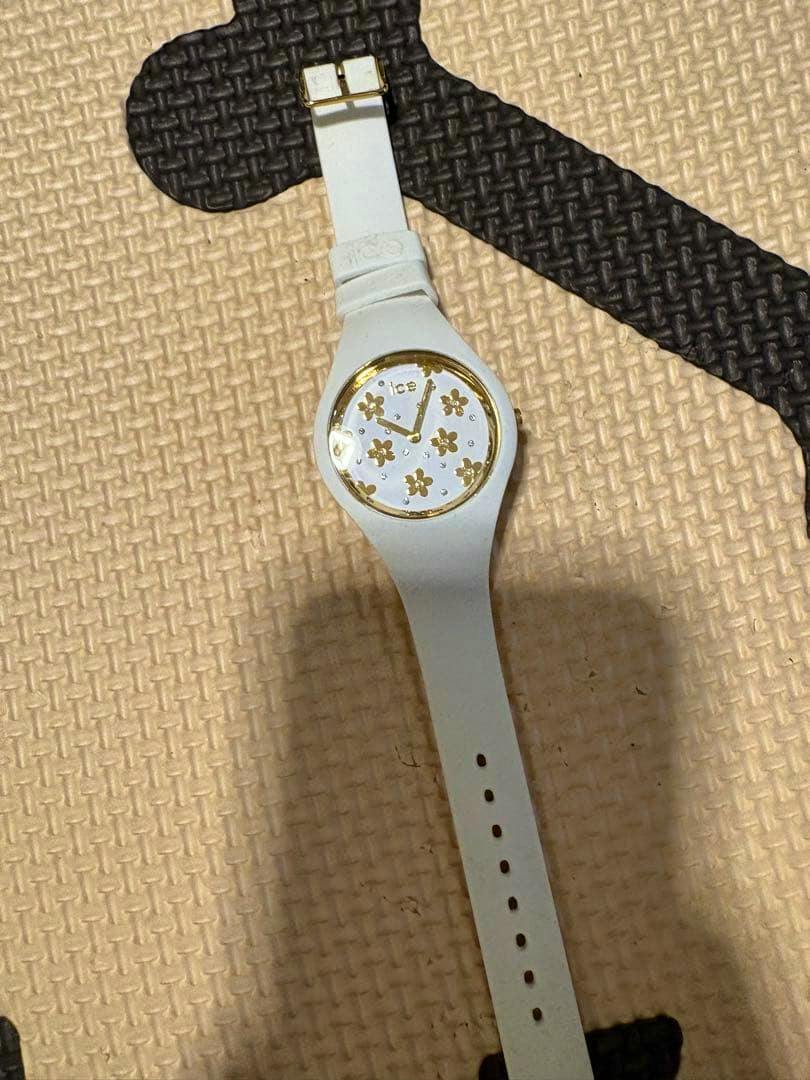 White Ice-Watch wristwatch with gold flower-pattern dial and white silicone strap on a textured mat.