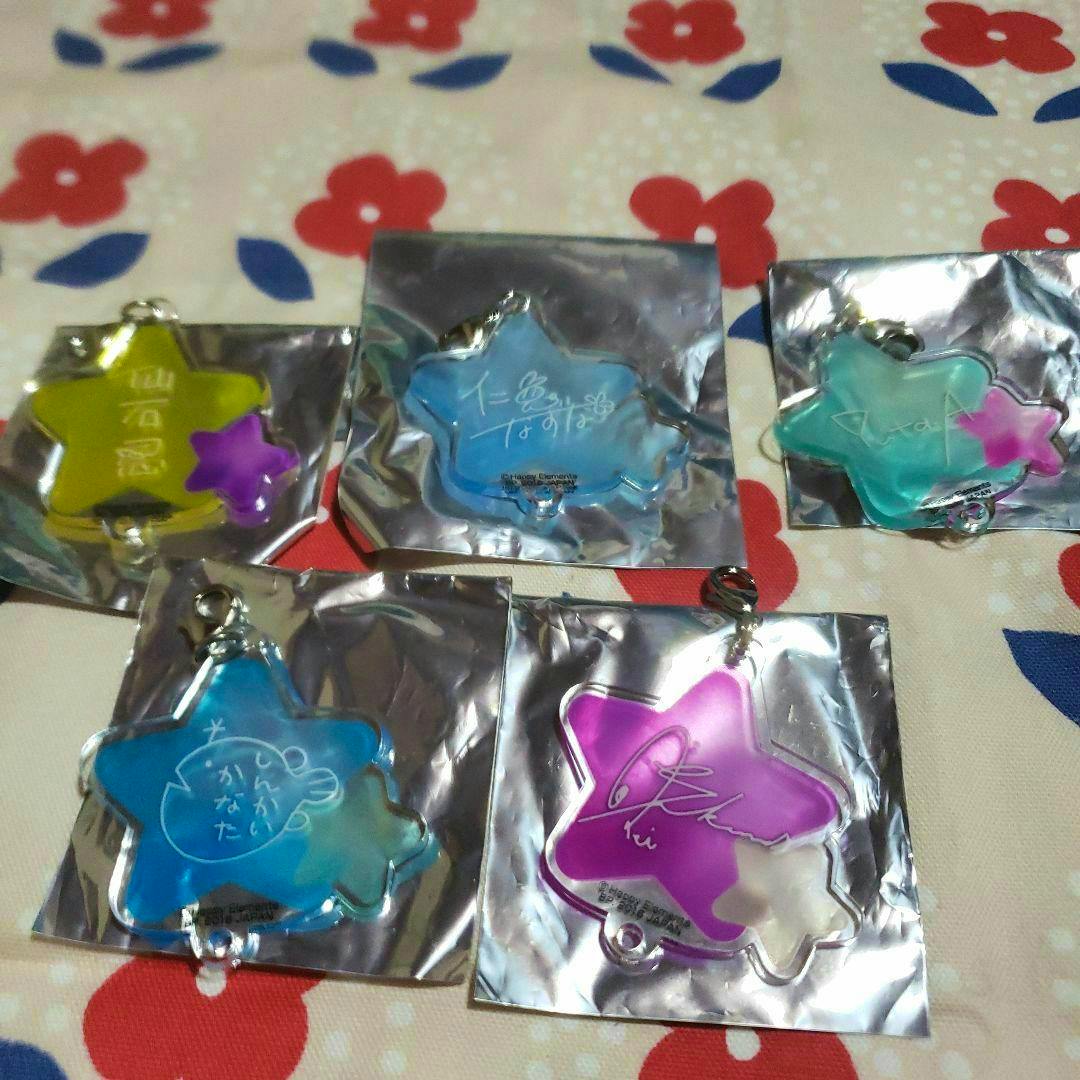 Five star-shaped acrylic keychain charms in different colors with printed signatures, displayed on silver foil backing over floral fabric.