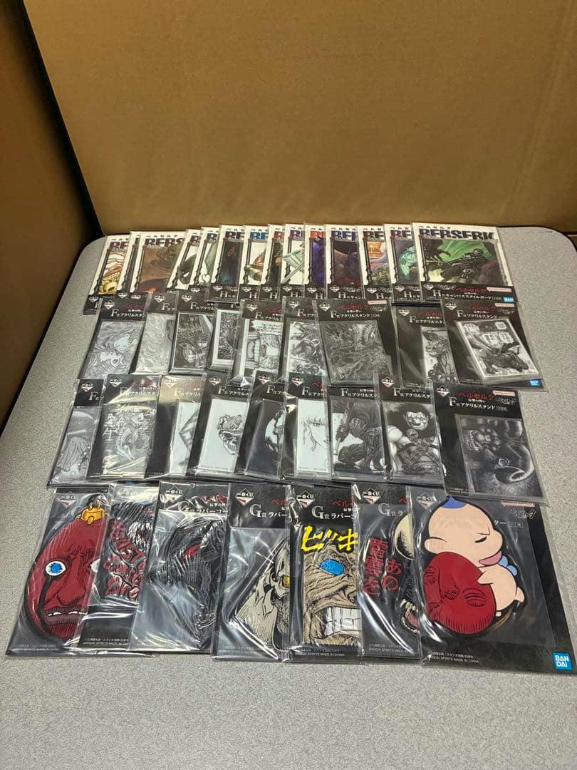 A laid-out collection of Berserk Ichiban Kuji F, G, and H prize items in their sealed packaging displayed on a table.