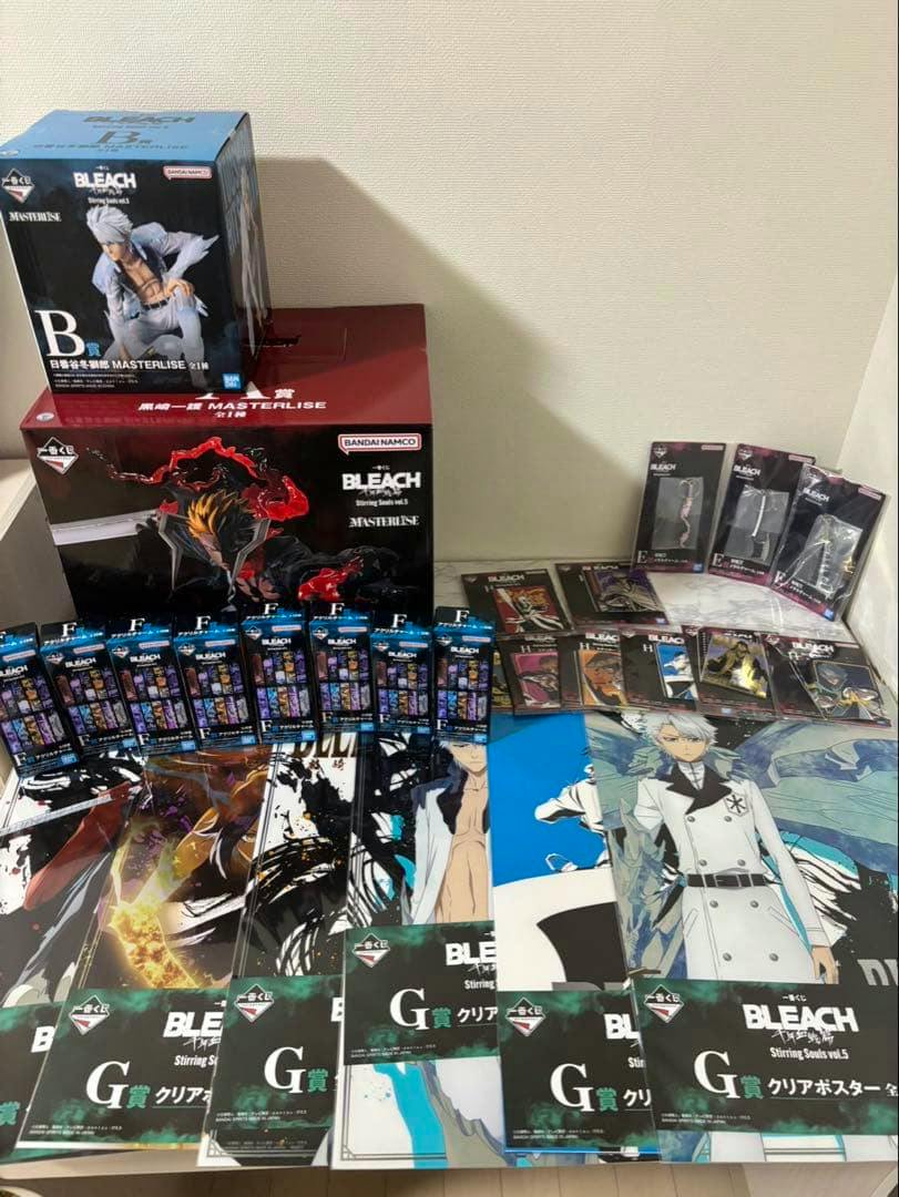 Photo showing BLEACH figure boxes with multiple clear posters and small packaged accessories arranged on a table.
