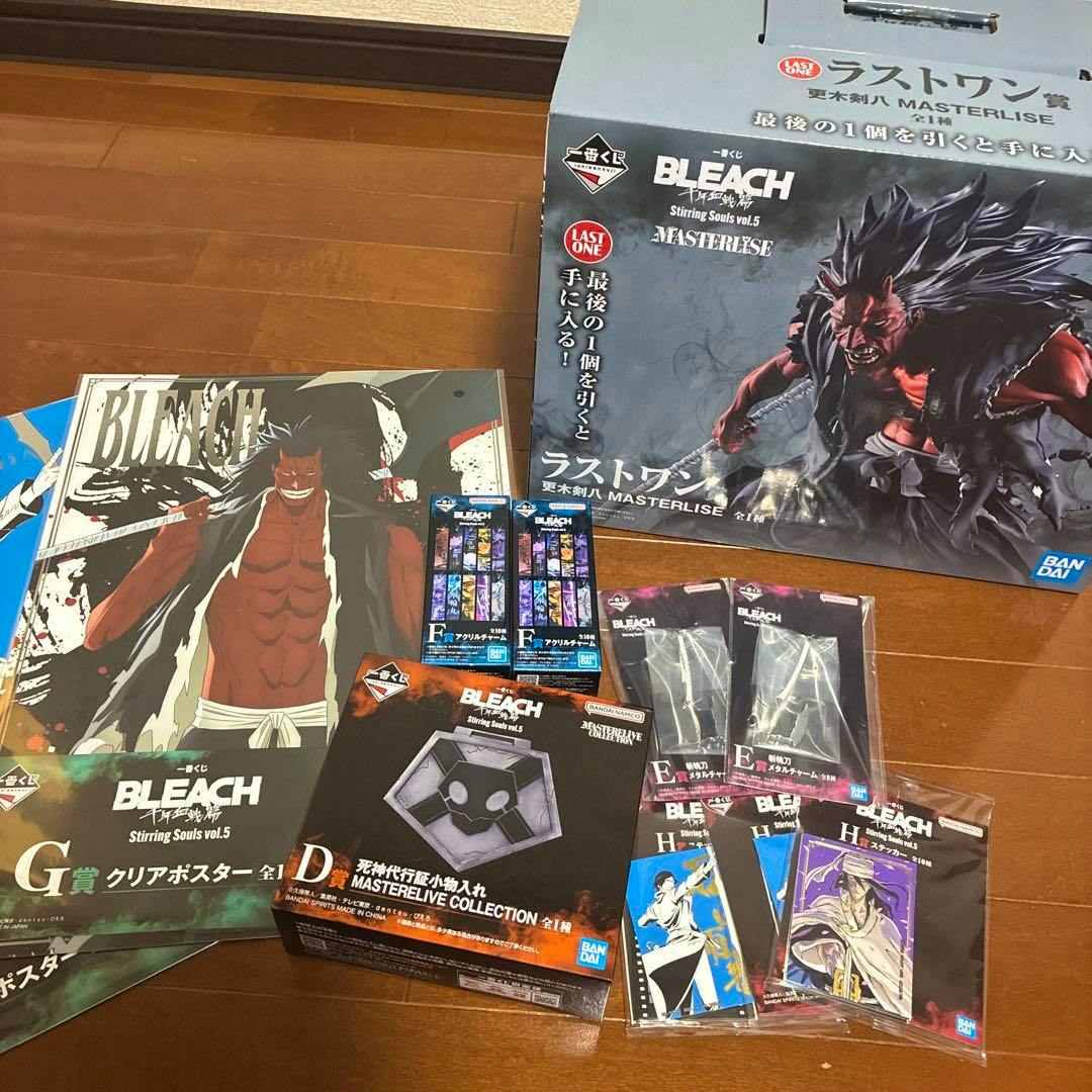 Photo of BLEACH Ichiban Kuji prize items laid out on a wooden floor, including the large Last One prize box, a D prize box, and multiple E-prize packaged items.