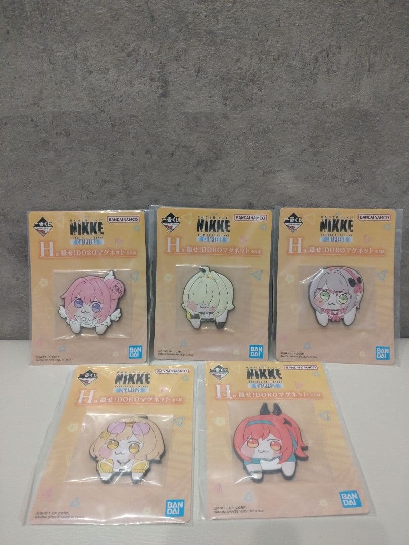 Five unopened NIKKE H-prize "Hide Doro" fridge magnets in their original packaging arranged on a flat surface.