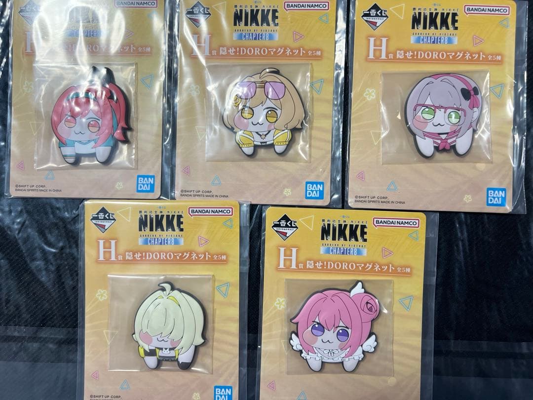 Photo of five packaged NIKKE DORO fridge magnets (5-piece set) displayed on a dark background.