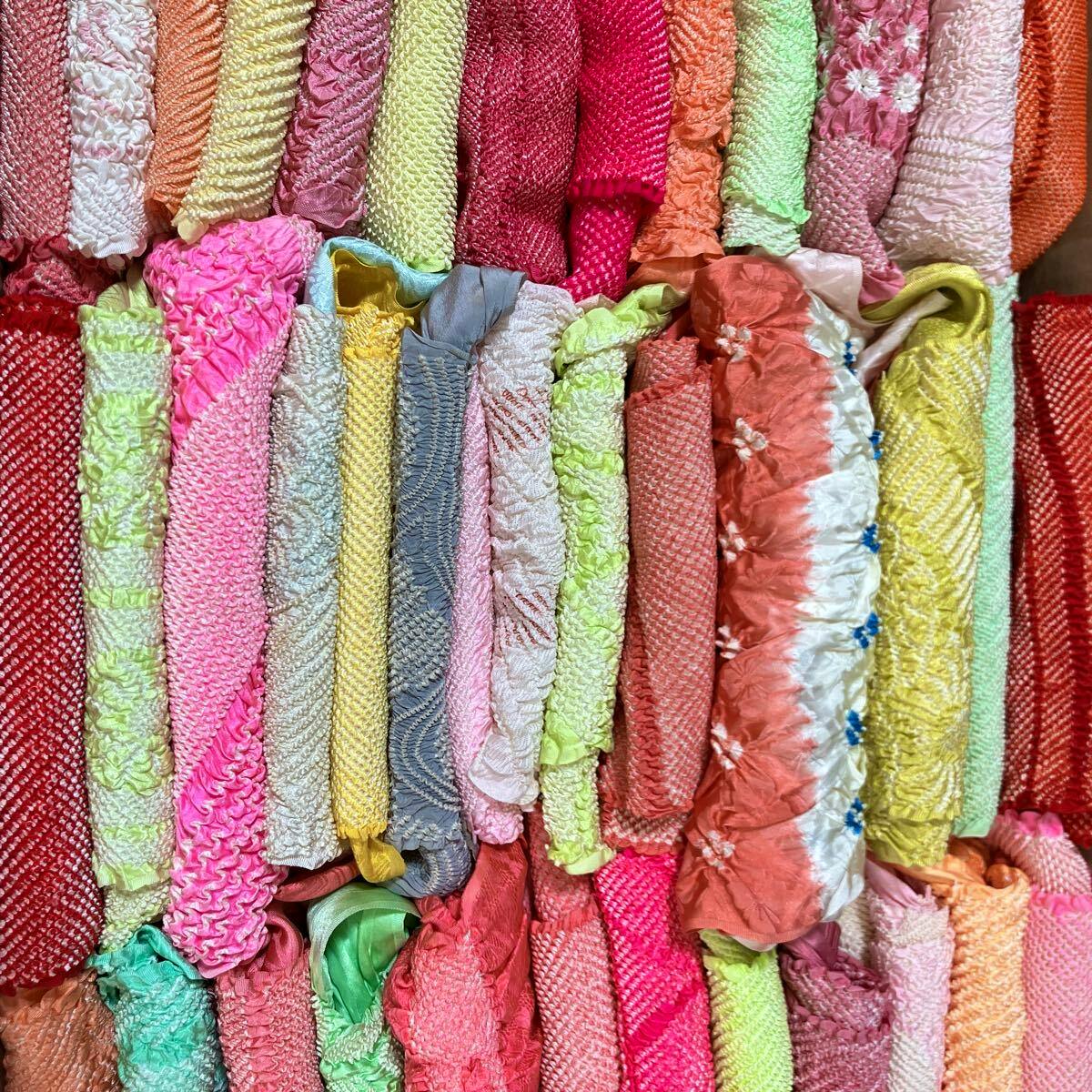 Multiple folded colorful shibori-style obiage (kimono sash scarves) arranged tightly in rows.